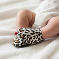 Baby wearing leopard print shoes on white blanket