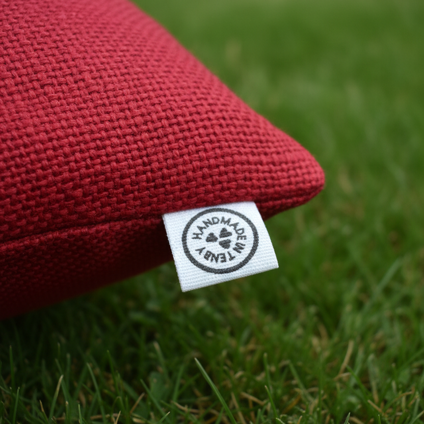 Handmade in Tenby Label on Red Cushion on Grass