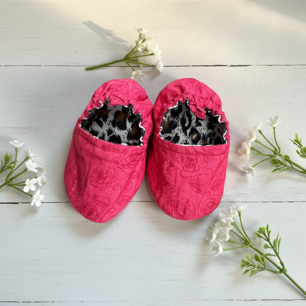 Pink roses baby shoes top-down on white wood with flowers