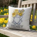 Tenby daffodil gnome cushion in a garden with daffodils